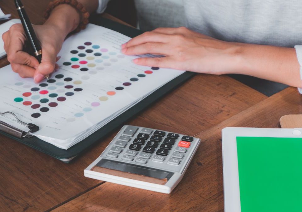 Un indépendant gère ses factures sur une table en bois avec une feuille et une calculatrice.